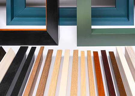 Campionario di listelli e aste in legno per la realizzazione di cornici artigianali su misura nel laboratorio.